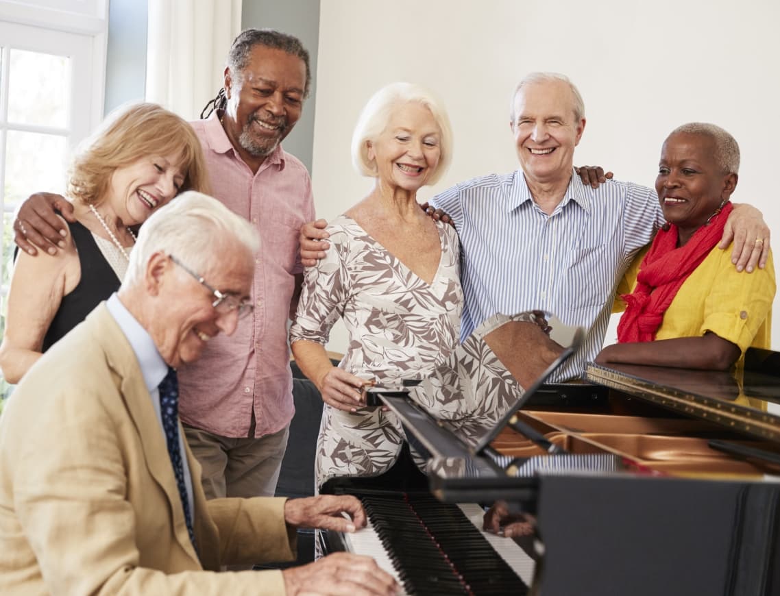Happy group of seniors watching man play piano at their senior living community.