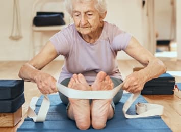 Elderly woman stretching with exercise strap during community fitness class at their senior living community