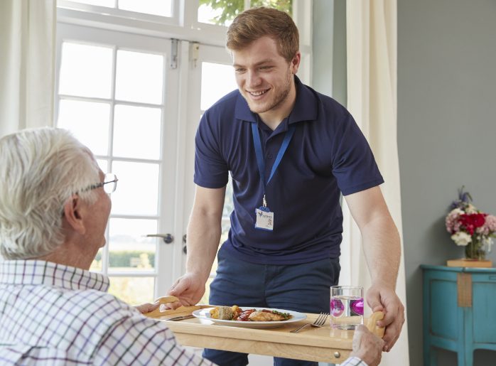 Happy caregiver serving a meal to a senior man.