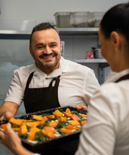 Smiling chef inspecting a tray of food.