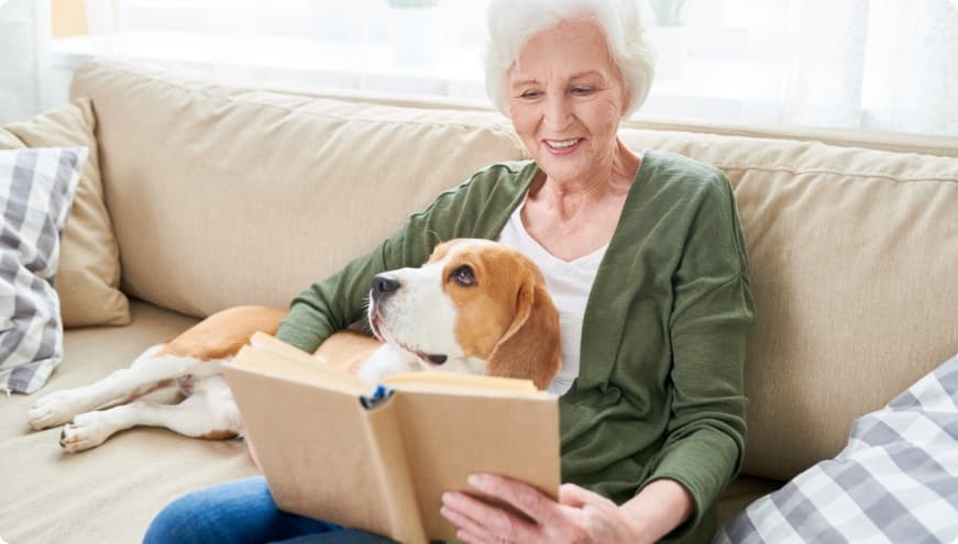 Senior woman reading a book, her dog sitting in her lap.