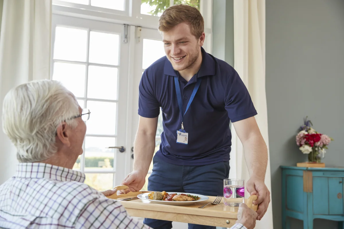 male care worker serving dinner to a senior resident